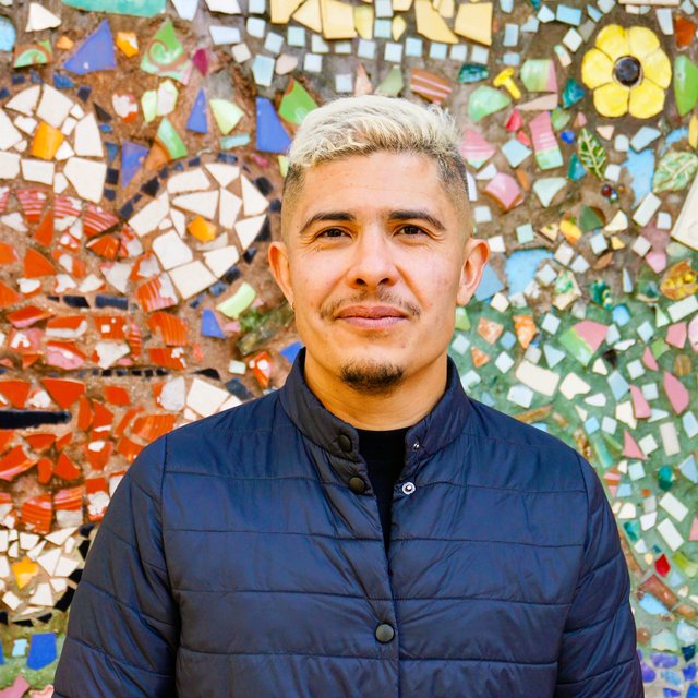 Roman Pérez, Founder and Principal of BODEGA LAND, in front of a colorful community tile mosaic.